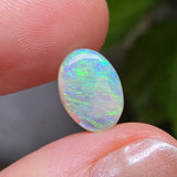 Opal stone held between fingers with a blurred green leafy background