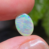 Opal stone held between fingers with a blurred green background