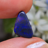 Blue gemstone held between two fingers with a blurred natural background