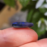Blue stone held between fingers with a blurred natural background
