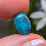 Blue opal stone held between fingers with a blurred natural background