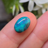 Opal stone held between fingers with a blurred natural background