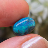 Blue opal stone held between fingers with a blurred natural background