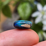 Blue stone held between fingers with a blurred natural background