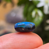 Blue stone held between fingers with a blurred natural background