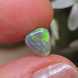 Opal stone held between fingers with a blurred natural background