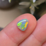 Opal stone held between fingers with a blurred natural background