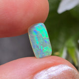 Opal stone held between fingers with a blurred natural background