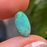Opal stone held between fingers with a blurred natural background