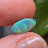 Opal stone held between fingers with a blurred natural background