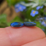 Two blue stones held between fingers with a blurred natural background