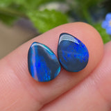 Two blue opal stones held between fingers with a blurred natural background