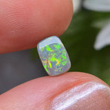 Opal stone held between fingers with a blurred natural background