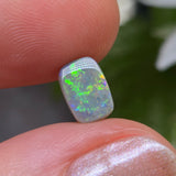 Opal stone held between fingers with a blurred natural background