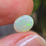 Opal stone held between fingers with a blurred natural background