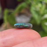 Opal stone held between fingers with a blurred green plant background