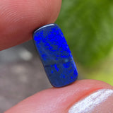 Blue opal stone held between fingers with a blurred green background