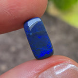 Blue gemstone held between two fingers with a blurred natural background
