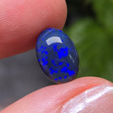 Blue glass gemstone held between fingers with a blurred green background